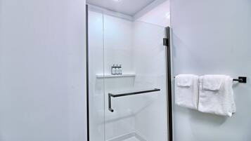 Un baño moderno con cabina de ducha de vidrio, un perchero con dos toallas y un estante con artículos de aseo.