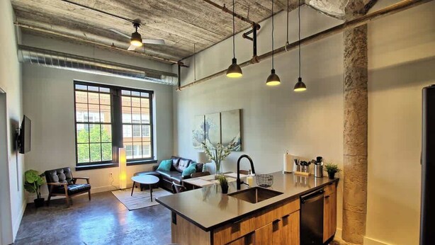 A spacious kitchen with a large island, pendant lighting, and a view of the outdoors through large windows. - Chic Ultramodern Loft w/ Designer Features+WD (Saint Louis)