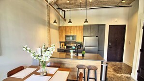 A modern kitchen with wooden cabinets, a central island, and a dining area with a wooden table and chairs. - Chic Ultramodern Loft w/ Designer Features+WD (Saint Louis)