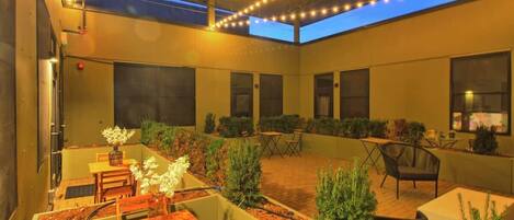 Un área de patio al aire libre con mesas y sillas, un tragaluz y luces colgantes.