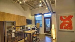 A modern kitchen with stainless steel appliances, a wooden countertop, and a bar area with stools. - Chic Ultramodern Minimalist Studio Loft + Patio (Saint Louis)