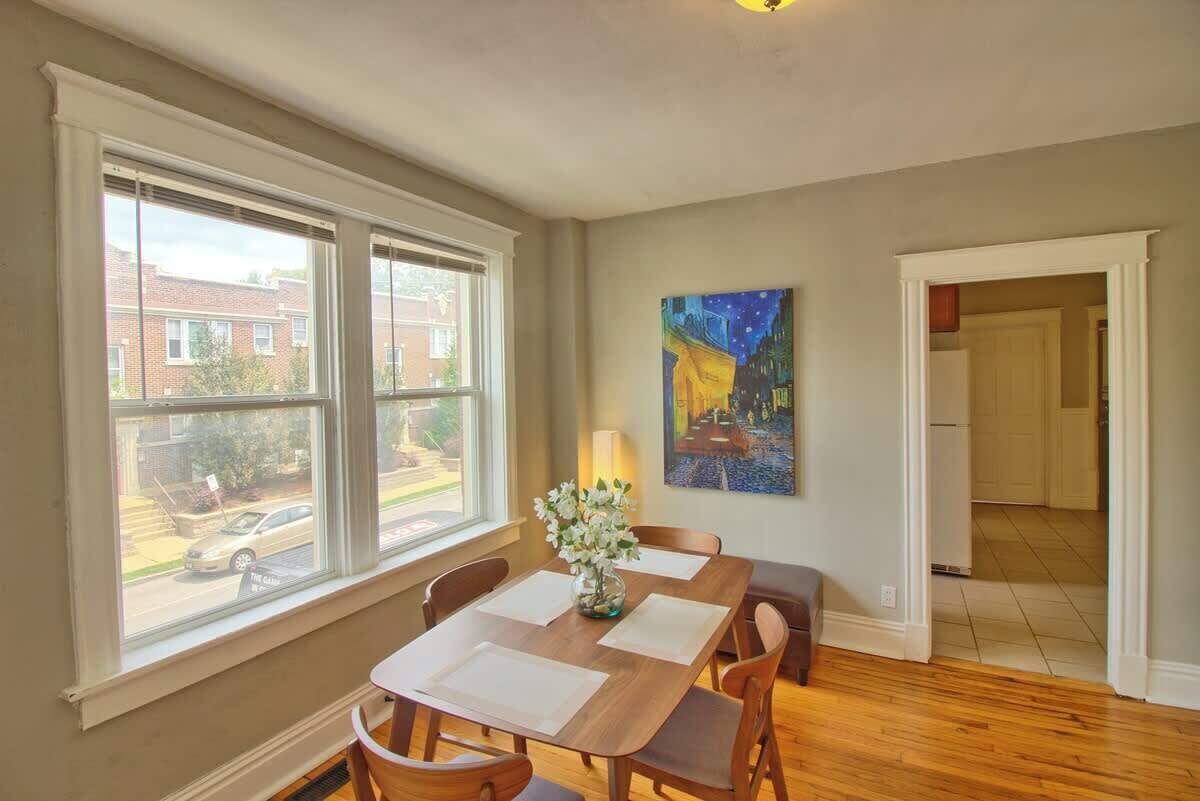 Un coin repas comprenant une table, des chaises, un vase de fleurs, un tableau accroché au mur et une vue dégagée grâce à de grandes fenêtres.