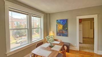 Un coin repas comprenant une table, des chaises, un vase de fleurs, un tableau accroché au mur et une vue dégagée grâce à de grandes fenêtres.