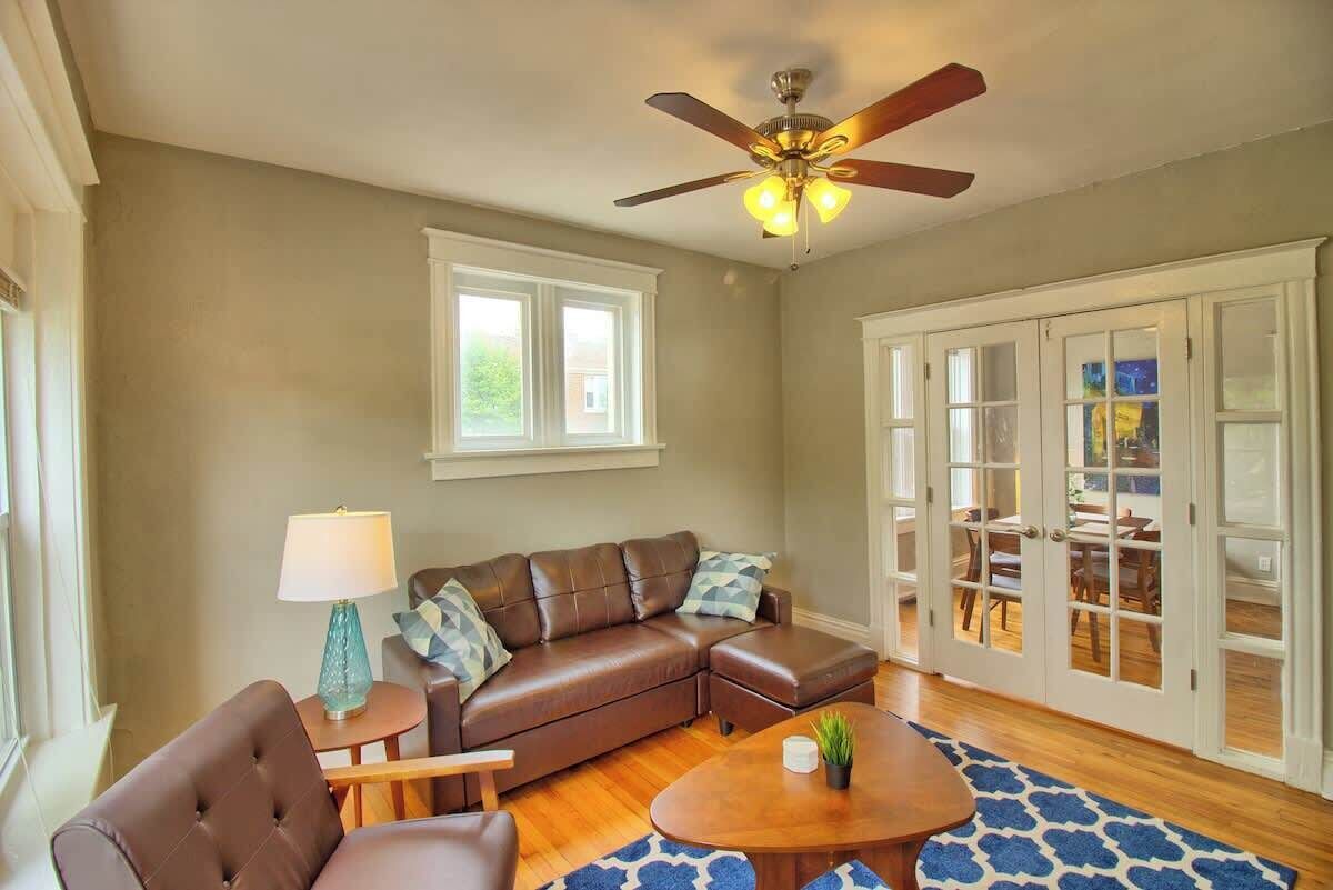 A living room with a brown leather sofa, a coffee table, a ceiling fan, and a view through glass doors to an outdoor area.