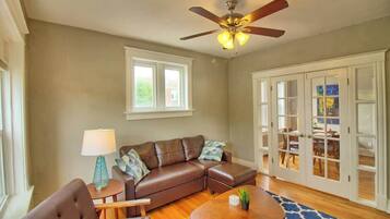 A living room with a brown leather sofa, a coffee table, a ceiling fan, and a view through glass doors to an outdoor area.