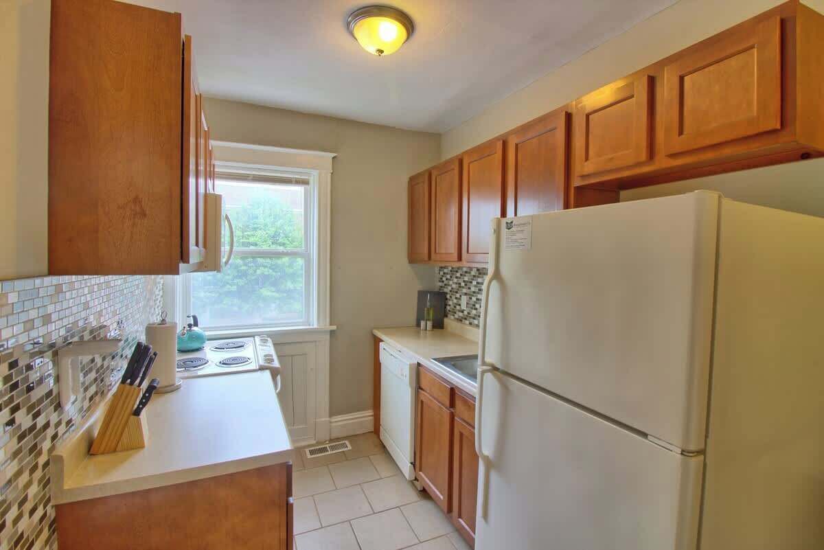 A kitchen with wooden cabinets, a white refrigerator, a window, and a tiled backsplash.
