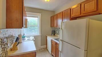 A kitchen with wooden cabinets, a white refrigerator, a window, and a tiled backsplash.