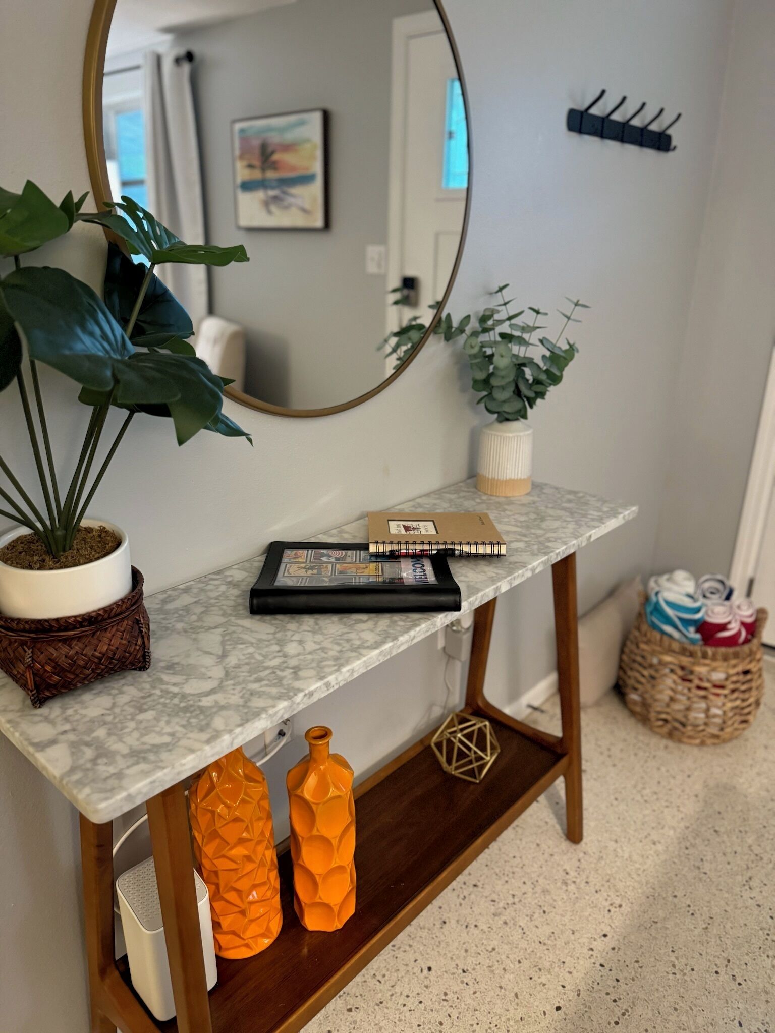 A marble console table with a mirror, a potted plant, a notebook, and decorative orange vases.