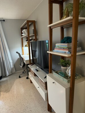 Un salon moderne avec un téléviseur à écran plat, des étagères en bois, un bureau et une chaise.