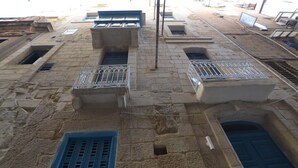 Un bâtiment en pierre avec des portes et des fenêtres bleues, doté de balcons ornés de rampes en métal.