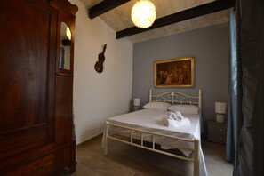 A bedroom with a bed, a wooden wardrobe, a violin, and a painting on the wall.