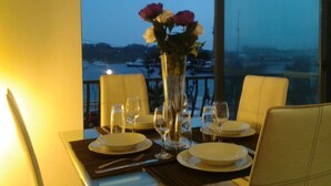 A dining table set for two with a vase of flowers, a view of a snowy landscape, and a railing in the background. - Water Front Flat - balcony (Tas-Sliema)