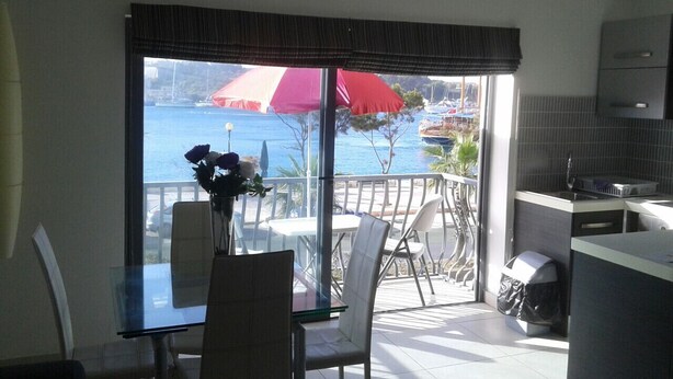 A balcony with a glass table and chairs, a red umbrella, and a view of the sea and boats. - Water Front Flat - balcony (Tas-Sliema)