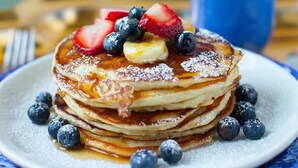 Una pila de panqueques con fresas, arándanos y jarabe en un plato.