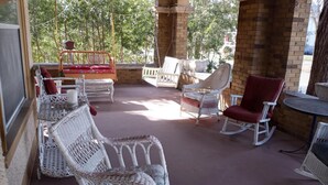 Un patio techado con mobiliario de mimbre, incluyendo una mecedora y sillones reclinables, además de un columpio.