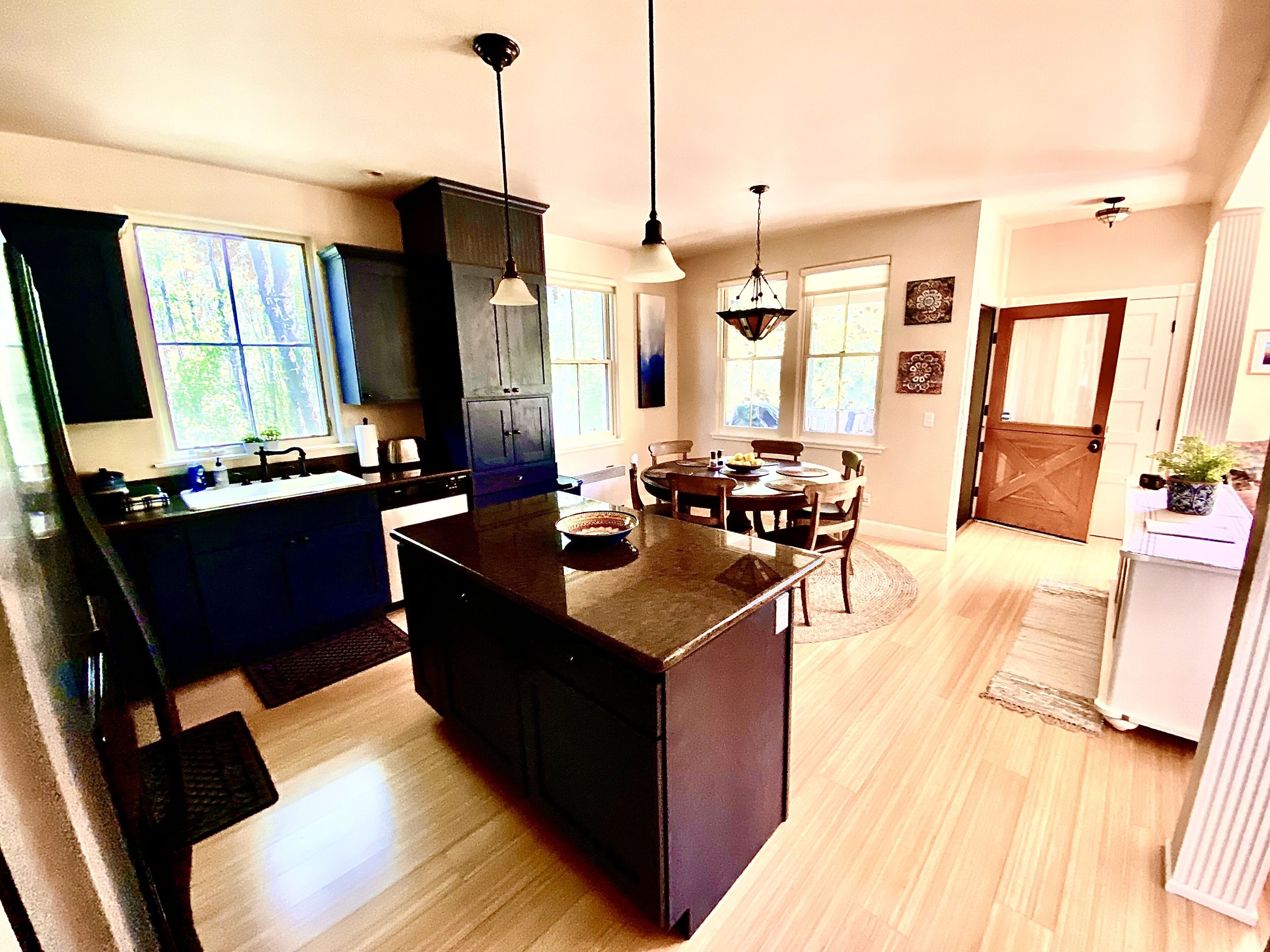 Une cuisine moderne dotée d’un îlot central, de meubles de couleur sombre et de luminaires suspendus.