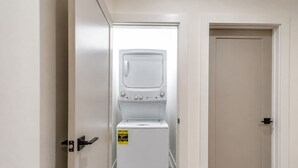 A laundry room with a white washing machine and dryer, a door with a handle, and a wall-mounted electrical outlet.