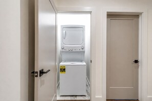 Un cuarto de lavado con lavadora y secadora blancos, una puerta con picaporte y un enchufe en la pared.