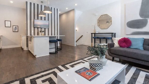 A modern living space with a kitchen island, bar stools, a sofa, and a coffee table with decorative items.