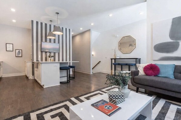 Un espacio habitable moderno con una isla de cocina, taburetes de bar, un sofá y una mesa de centro con objetos decorativos.