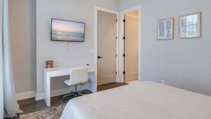Ein Schlafzimmer mit einem Bett, einem Schreibtisch, einem Sessel, einem Fernseher und zwei gerahmten Bildern an der Wand.