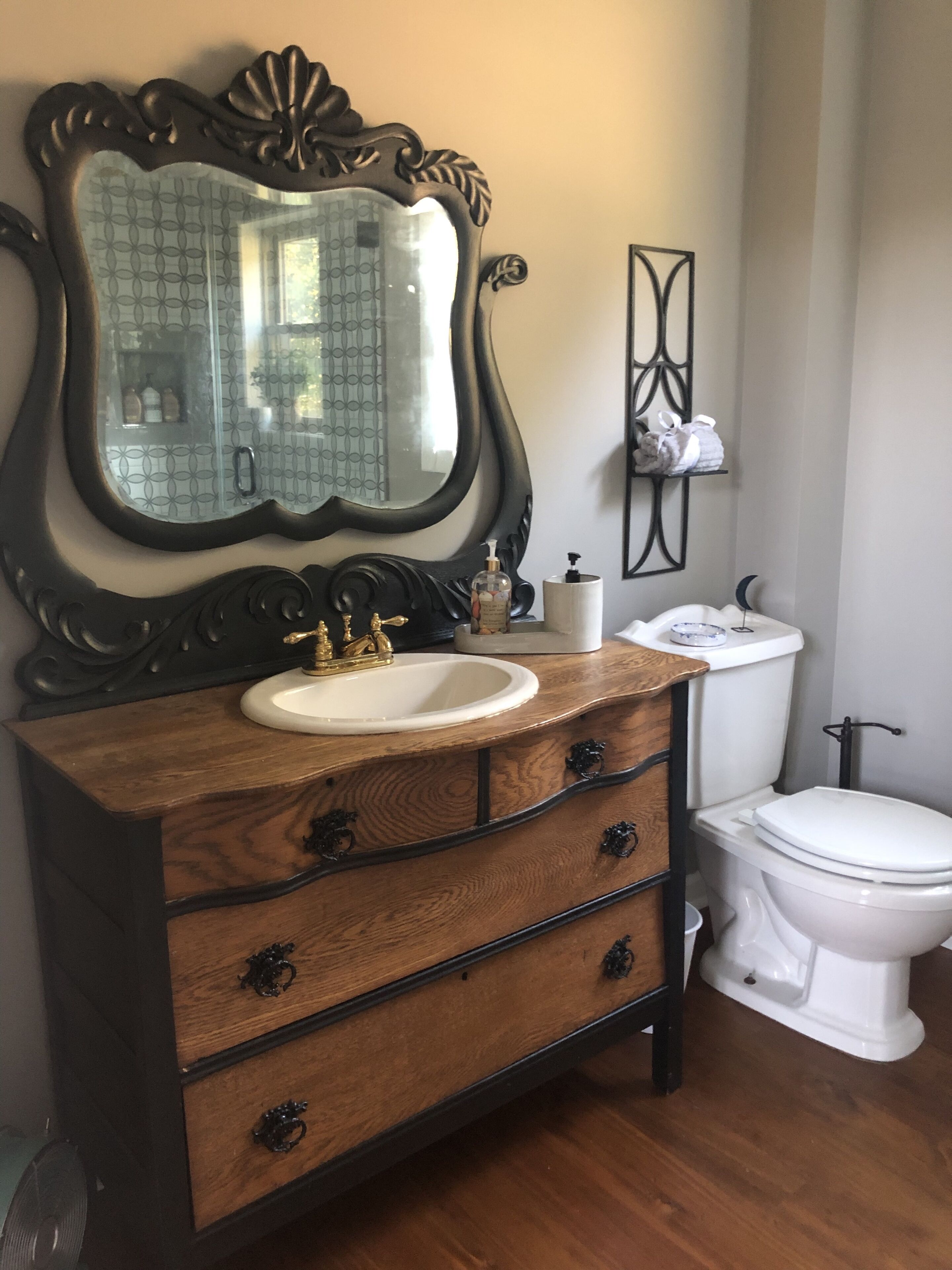 A bathroom with a wooden vanity, a large mirror, a sink, a toilet, and a small shelf with toiletries.