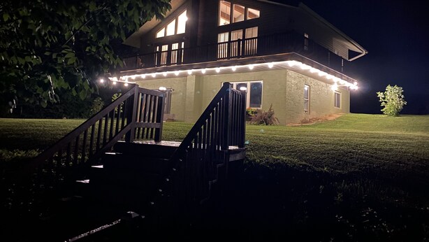 Ein zweistöckiges Haus mit einem Balkon, einer Veranda mit Treppe und Lichterketten.