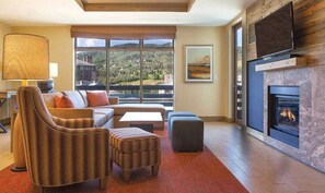 Relax in a cozy seating area with a sofa, armchairs, and a fireplace, taking in the scenic view of the hilly landscape.