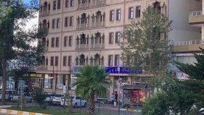 A multi-story building with balconies, a ground-level shop, and parked cars. - Tas Saray Bardakci Hotel (Kahta)
