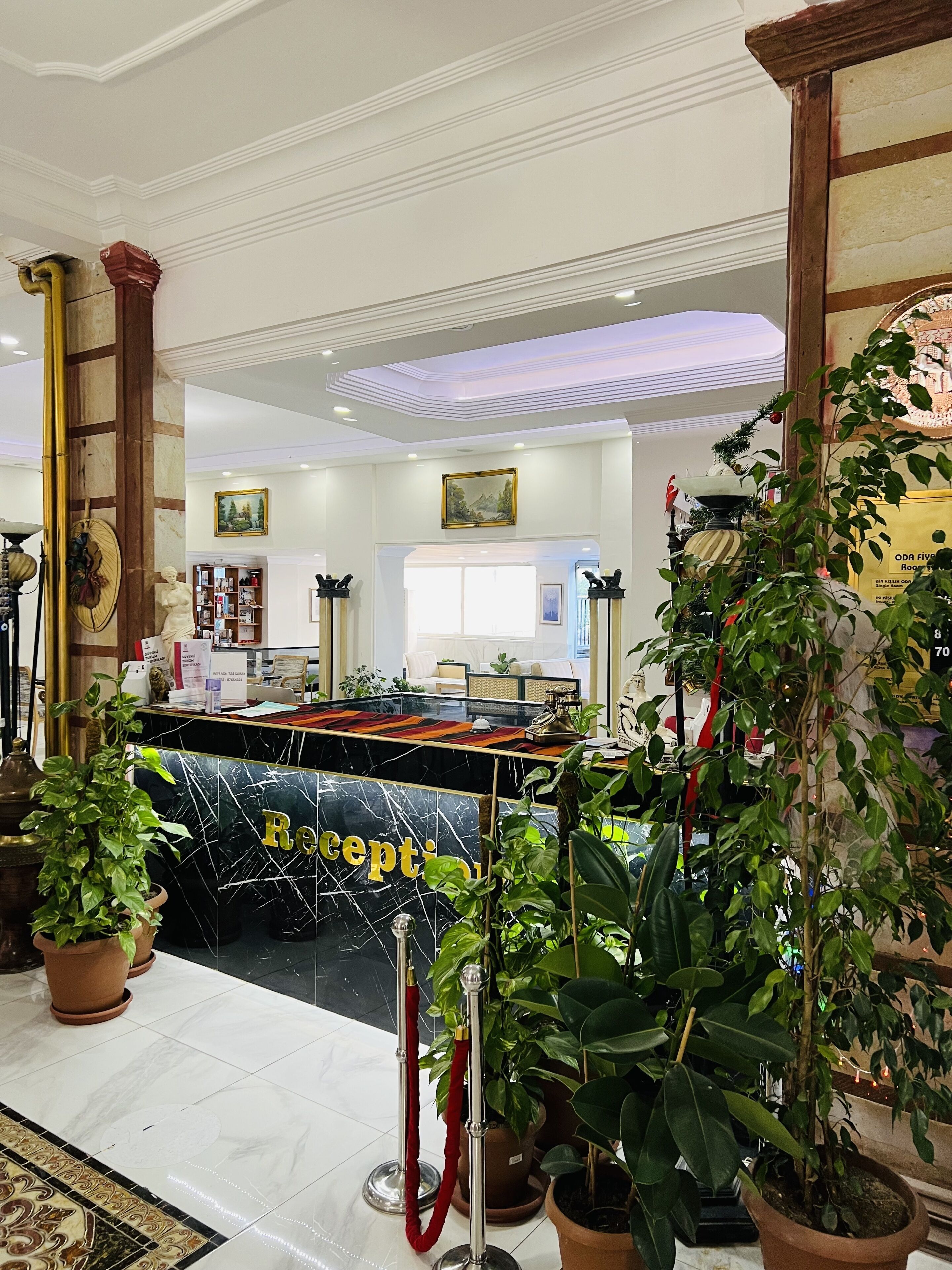 A reception area with a marble reception desk, potted plants, a red rope barrier, and a view of the lobby.