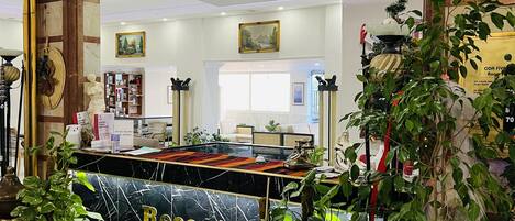 A reception area with a marble reception desk, potted plants, a red rope barrier, and a view of the lobby.