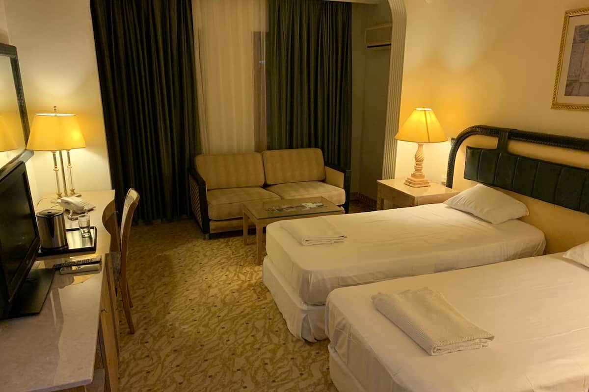 Een hotelkamer met twee bedden, een bank, een bureau met een televisie en lampen.