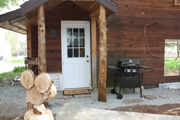 A wooden cabin with a white door, a barbecue grill, and a welcome mat.