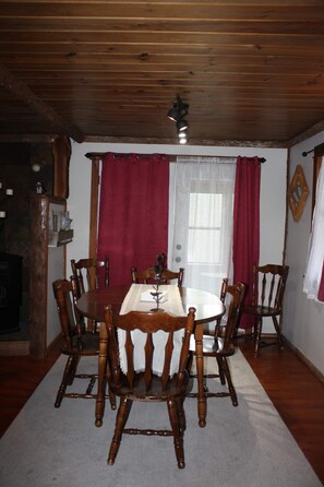 A dining room with a wooden table and chairs, a chandelier, and red curtains.