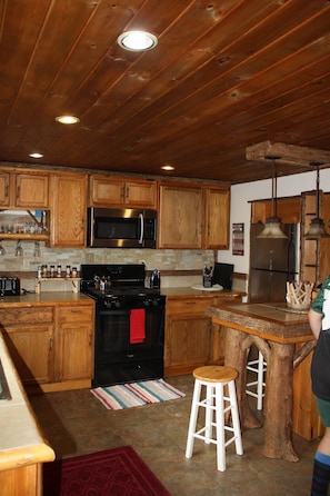 A kitchen with wooden cabinets, stainless steel appliances, and a tree stump bar.