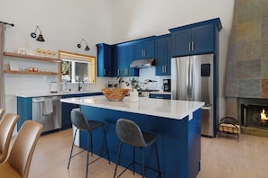A modern kitchen with blue cabinets, a stainless steel refrigerator, and a central island with bar stools. - Sunrise Chalet - Newly Remodeled Tahoe Donner Home with Game Room, Pool Table and Garage (Truckee)