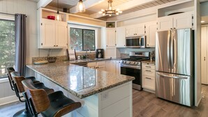 A modern kitchen with granite countertops, stainless steel appliances, and a bar area with bar stools. - Tahome Lodge - Dog Friendly Retreat with Private Hot Tub, Remote Workspace, Near Hiking (Truckee)