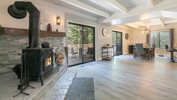 A spacious living area with a stone fireplace, wooden flooring, and a large sliding glass door leading to a deck. - Tahome Lodge - Dog Friendly Retreat with Private Hot Tub, Remote Workspace, Near Hiking (Truckee)