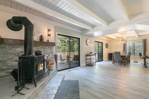 A spacious living area with a stone fireplace, wooden flooring, and a large sliding glass door leading to a deck. - Tahome Lodge - Dog Friendly Retreat with Private Hot Tub, Remote Workspace, Near Hiking (Truckee)