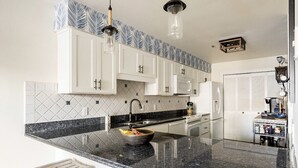 A kitchen with white cabinets, a granite countertop, and a hanging light fixture. - Captain’s Suite Beach Condo Near Rudee Inlet (Virginia Beach)