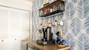 A kitchen with a coffee station, including a coffee maker, mugs, and shelves with kitchen items. - Captain’s Suite Beach Condo Near Rudee Inlet (Virginia Beach)