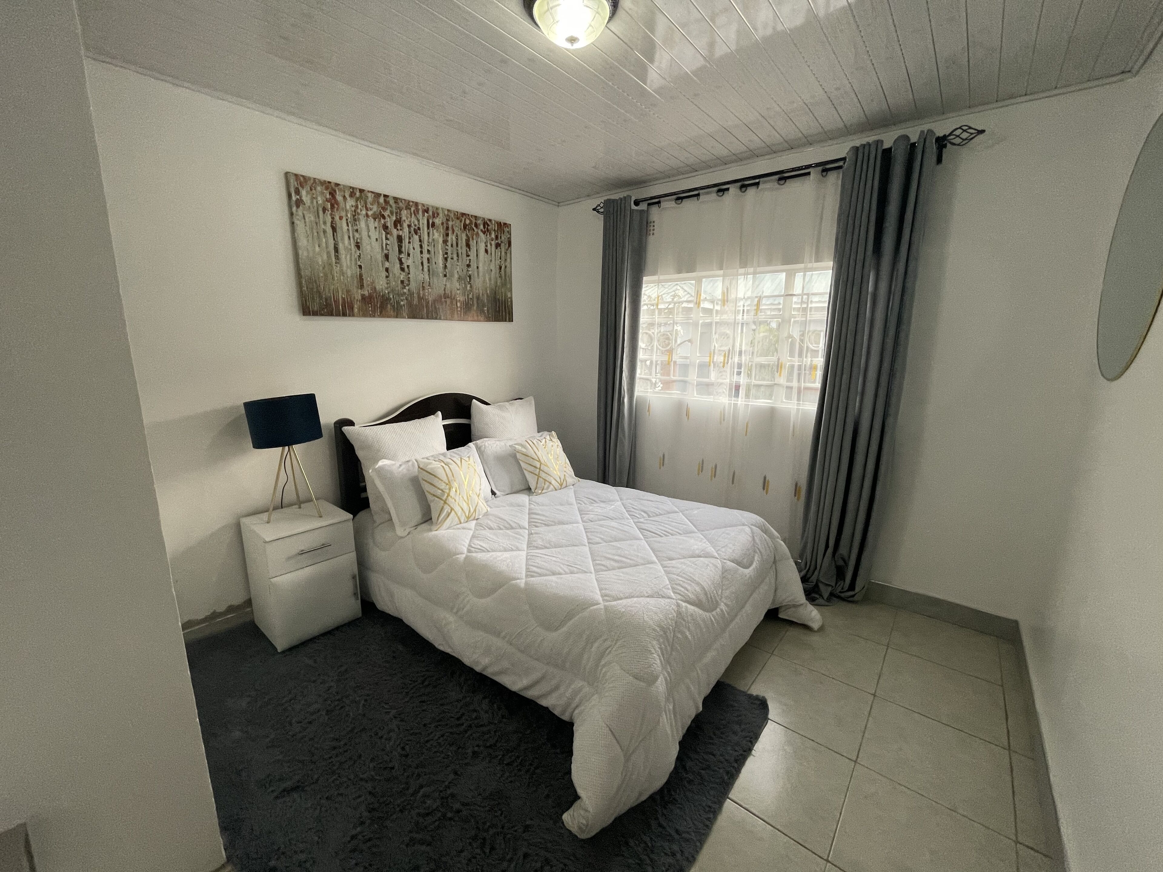A bedroom with a bed, nightstands, a lamp, a painting, and a window with curtains.