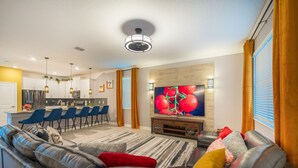 En moderne stue med en lædersofa, et fladskærms-tv og et spiseområde med blå stole.