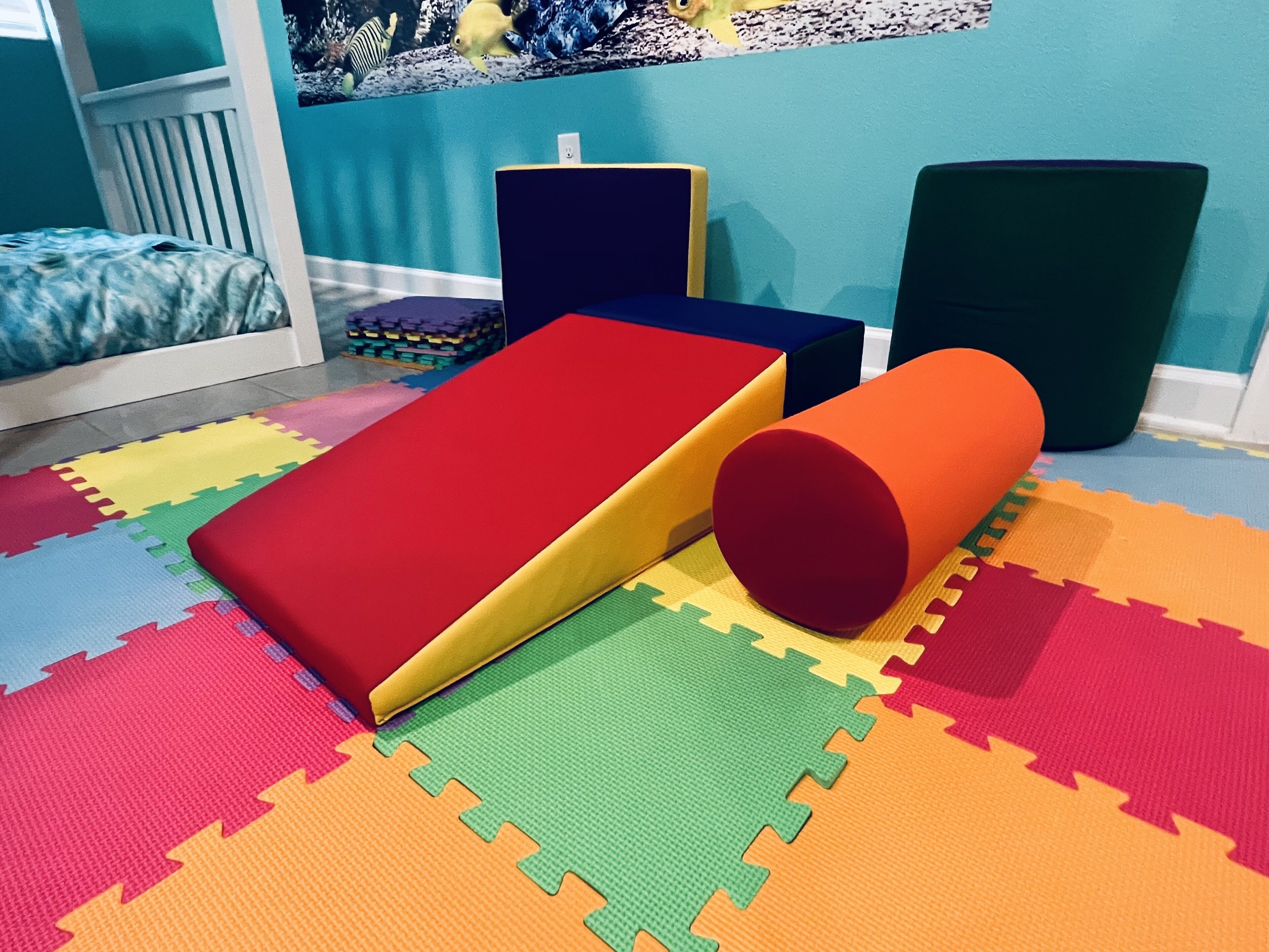 Un espace de jeux avec des tapis en mousse colorés, un toboggan et des blocs en mousse.