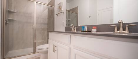 Un baño moderno con cabina de ducha, inodoro y tocador con un espejo grande.