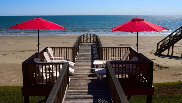 A wooden boardwalk leading to beach chairs and umbrellas with a view of the ocean.