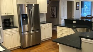 A modern kitchen with white cabinets, a stainless steel refrigerator, and a black countertop.