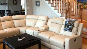 A spacious living room with a large L-shaped beige leather sofa, a black coffee table, and a wooden staircase with white balusters.