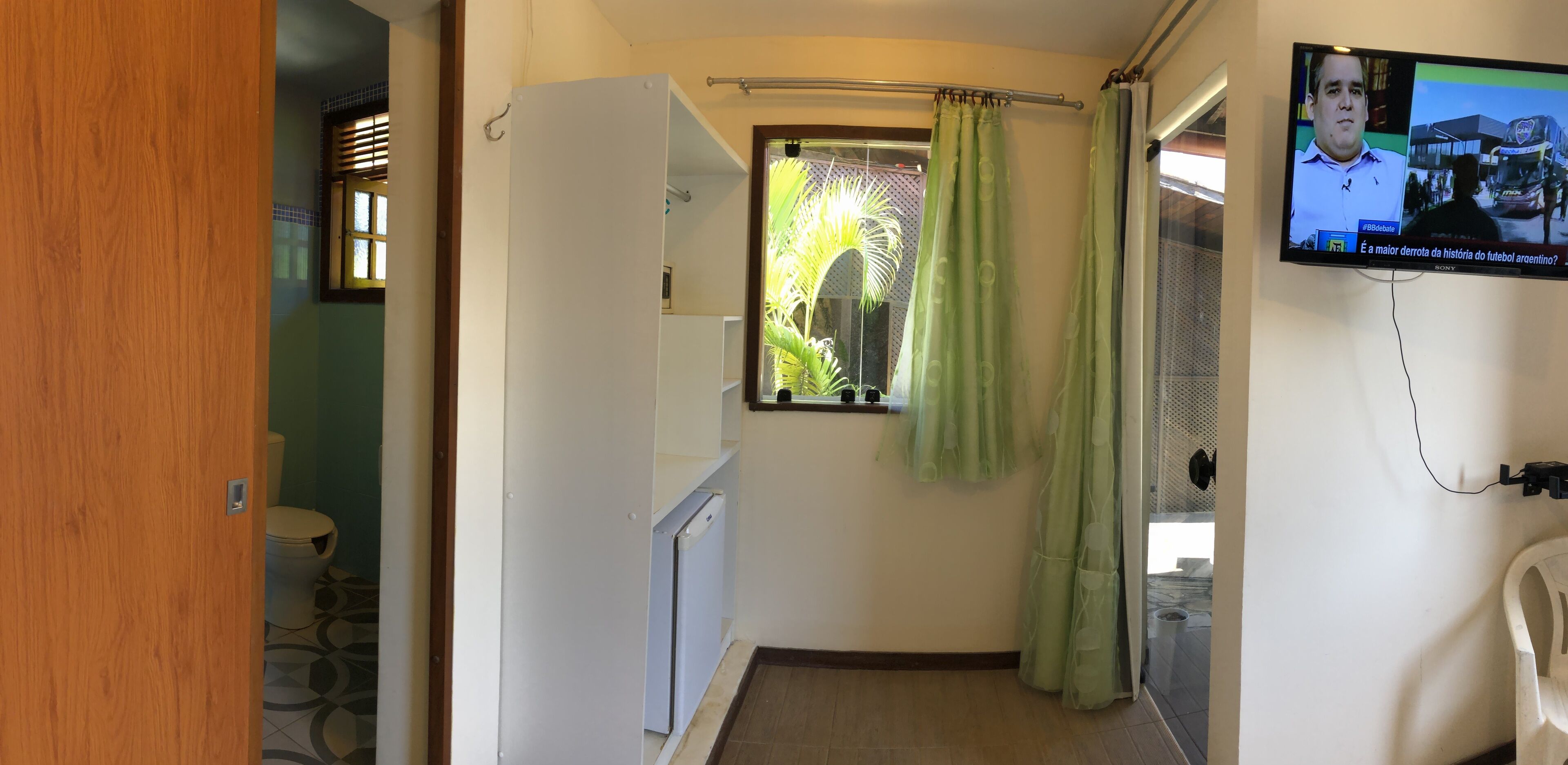 A bathroom with a toilet, a shower curtain, and a television mounted on the wall.