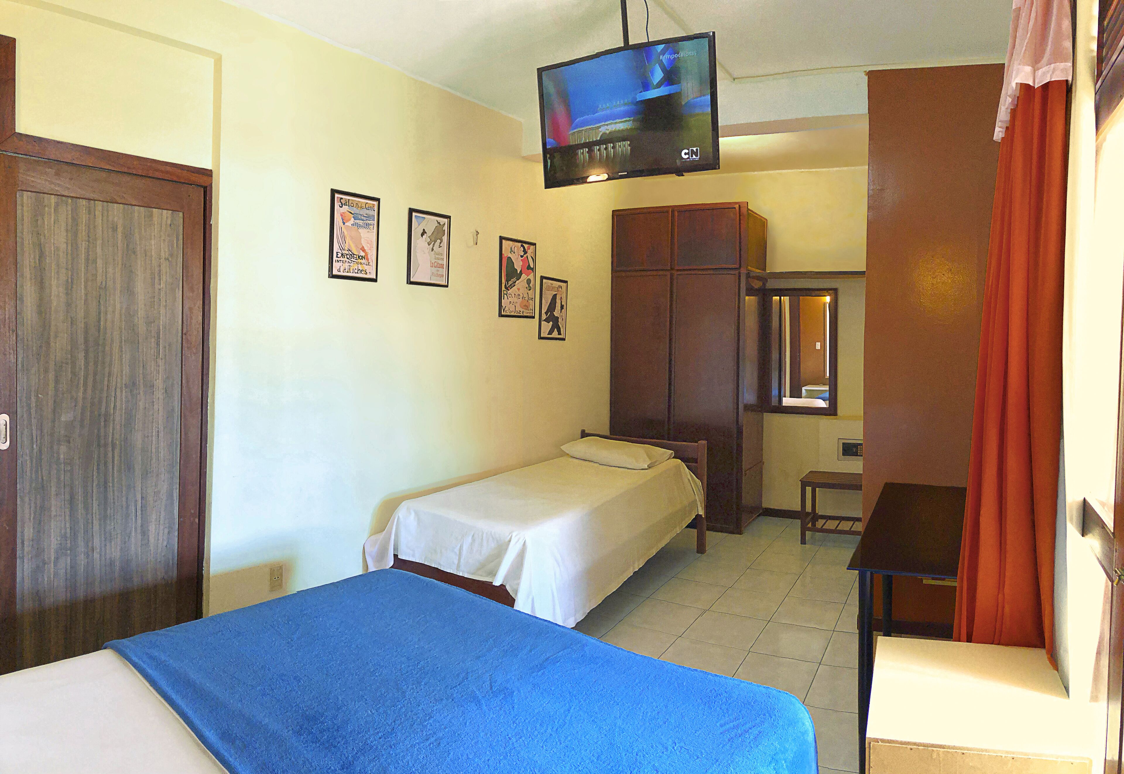 A hotel room with two single beds, a television, a wardrobe, and a small table.
